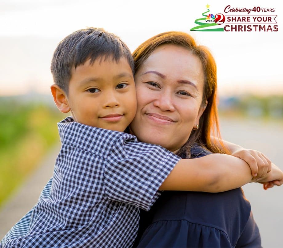 Smiling woman hugging a young boy outdoors at sunset.