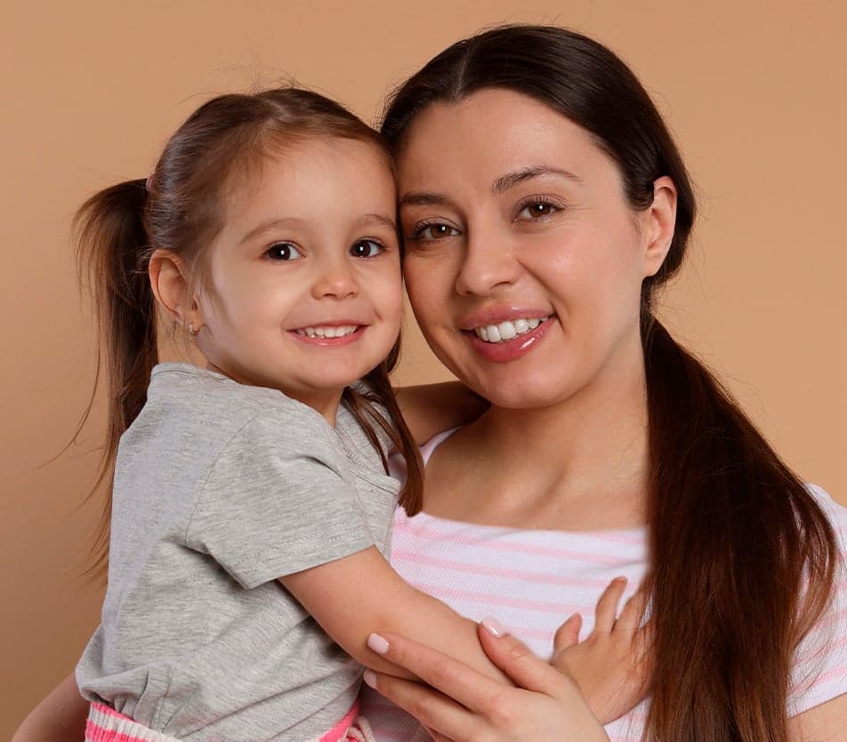 A smiling woman holds a young girl in her arms, both looking at the camera.